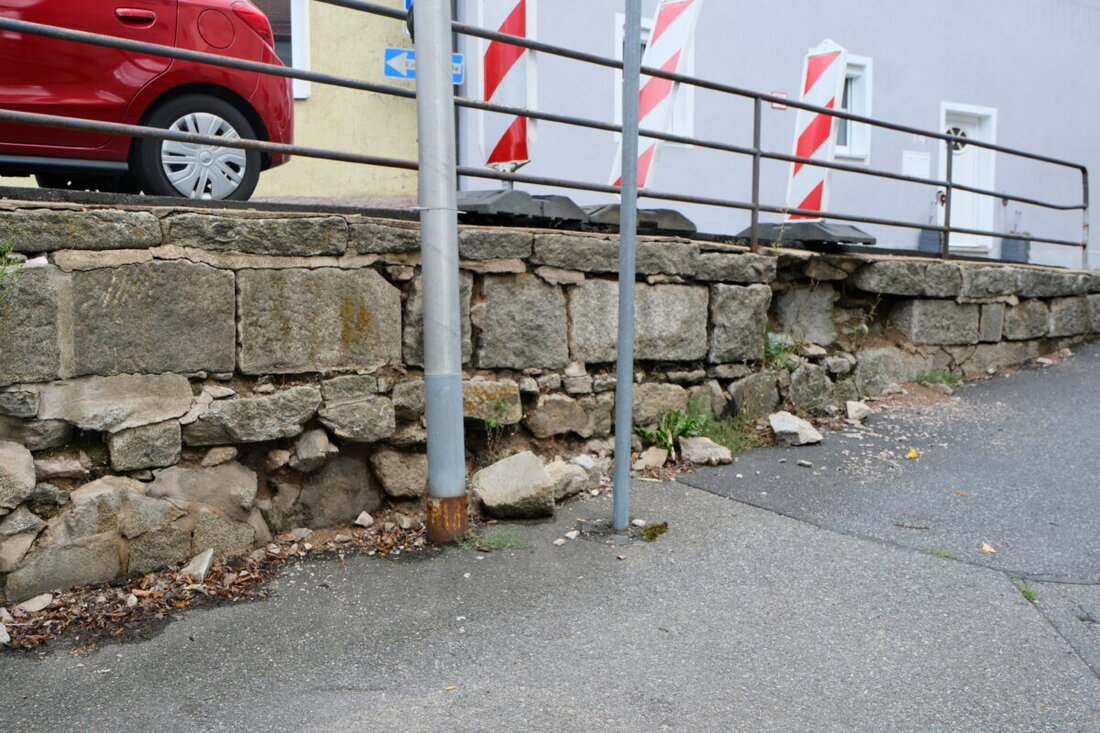 Floß. An der Synagoge gefährdet eine marode Granitmauer in der Bergstraße Fußgänger und Verkehr. Zugleich behindert ein Baugerüst seit Jahren die Straße. Bürgermeister Robert Lindner drängt auf die Sanierung bis Frühjahr 2027.
