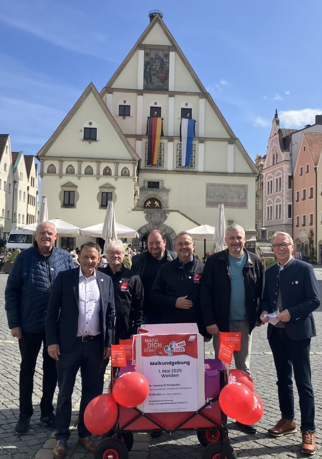 Weiden. Der DGB wirbt mit einem Bollerwagen in Weiden für die Maiveranstaltung 2025, verteilt Maiabzeichen und kündigt ein Programm mit Reden, Musik und Aktionen für den 1. Mai an.