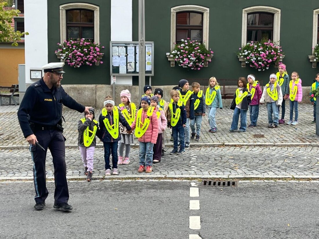 Eslarn. Mit leuchtend gelben, reflektierenden Dreieck-Überwürfen und praktischem Training von Verkehrserzieher Wolfgang Piehler lernen Erstklässler den sicheren Schulweg. Elternlotsen, Verkehrswacht und AOK erhöhen Sichtbarkeit.